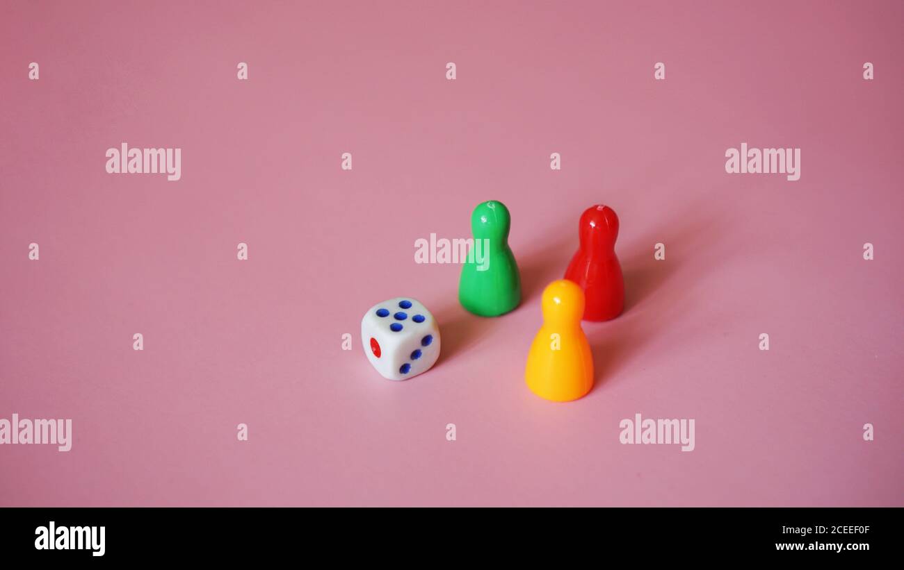 Board game figures and one dice on pink background Stock Photo
