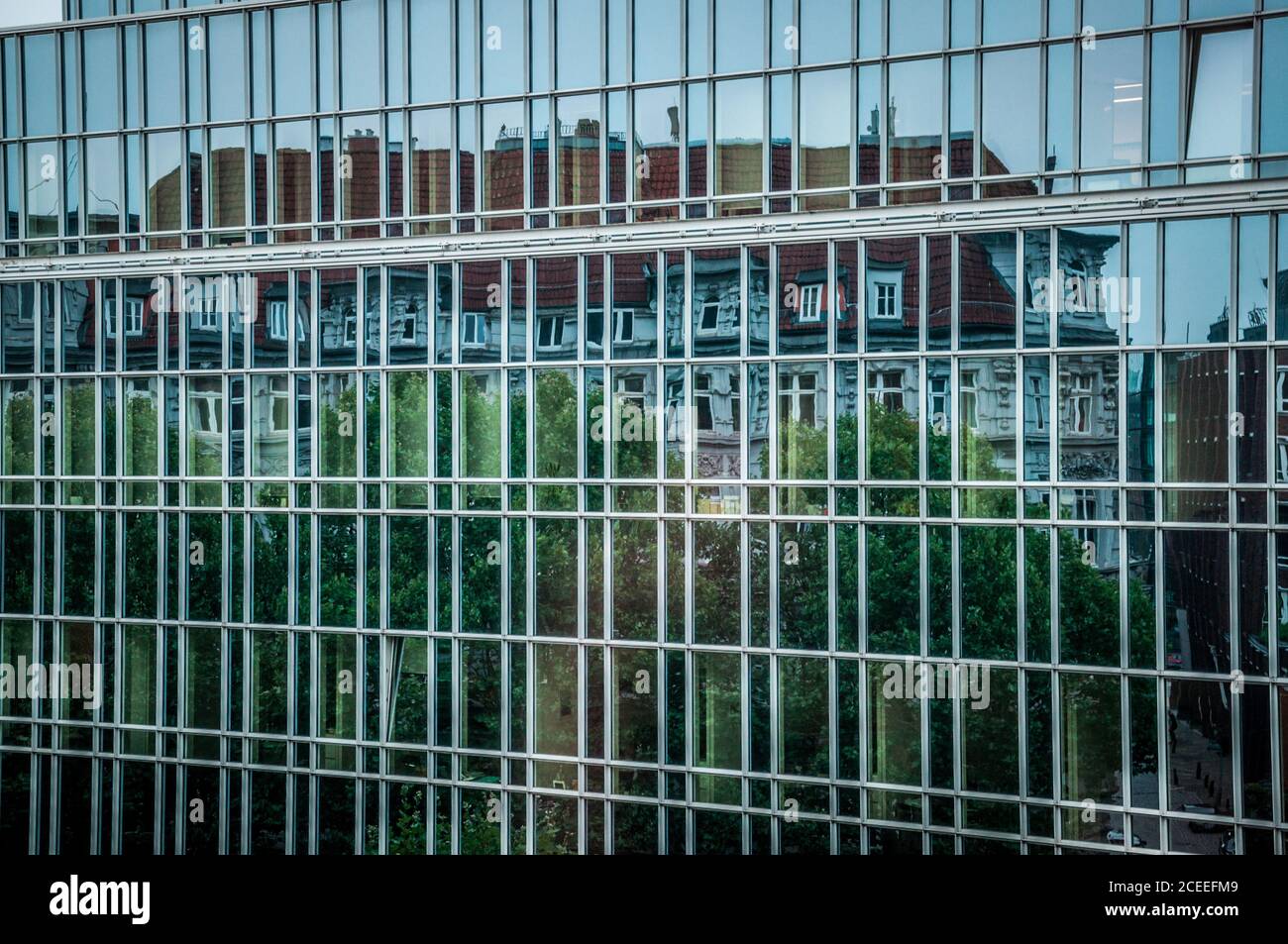 Framed glass wall of corporate building in Hamburg Germany. Distorted reflection of antique house rooftop in mirrored surface of modern architecture Stock Photo