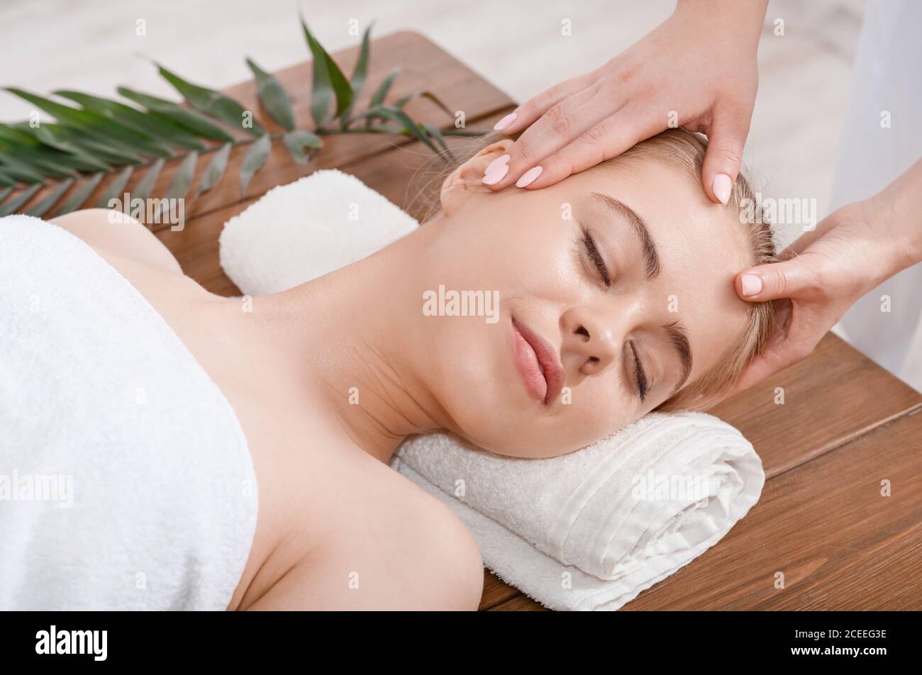 Female hands do rejuvenating face massage for woman on table with palm leaf Stock Photo