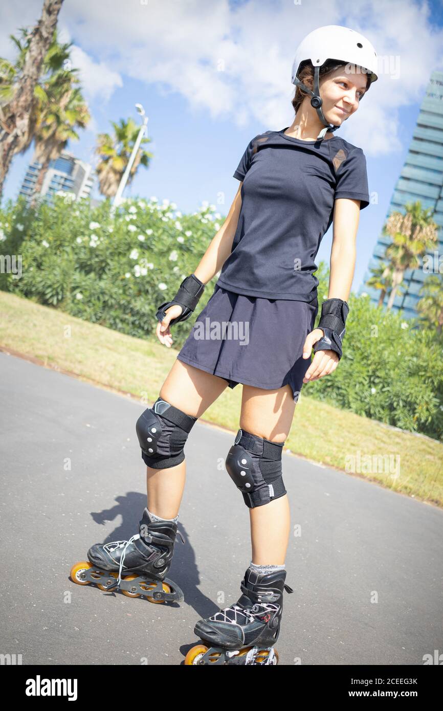 Young happy roller skater caucasian woman in the white helmet and black sporty clothes, sunny day, skatepark, urban environment. Stock Photo