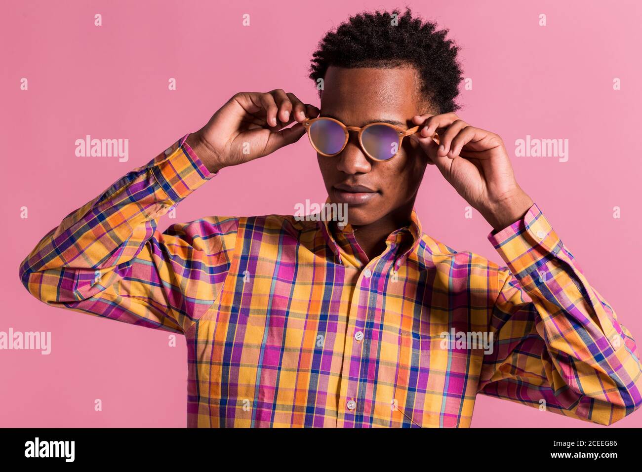 Trendy black man wearing colorful checkered shirt with shiny pink sunglasses standing on pink background Stock Photo