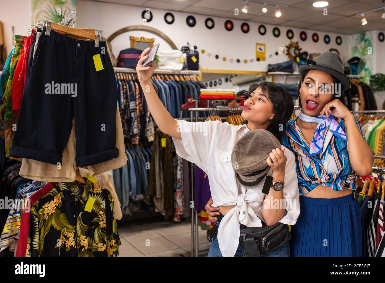 Cheerful friends trying on hat in shop and taking selfie Stock Photo