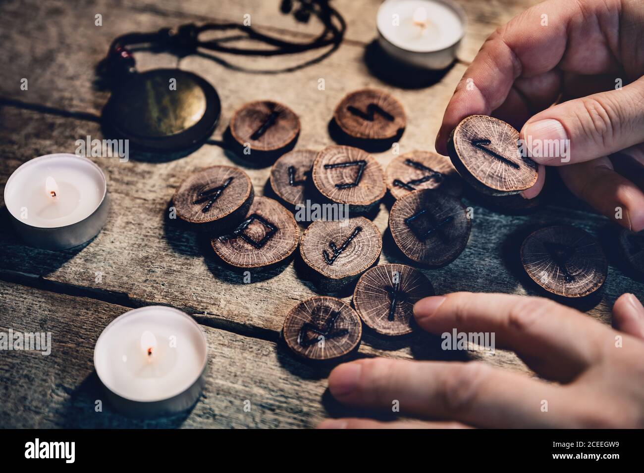 Hand holding wooden runes, esoteric and spirituality, reading and fortuneteller, details with candles Stock Photo