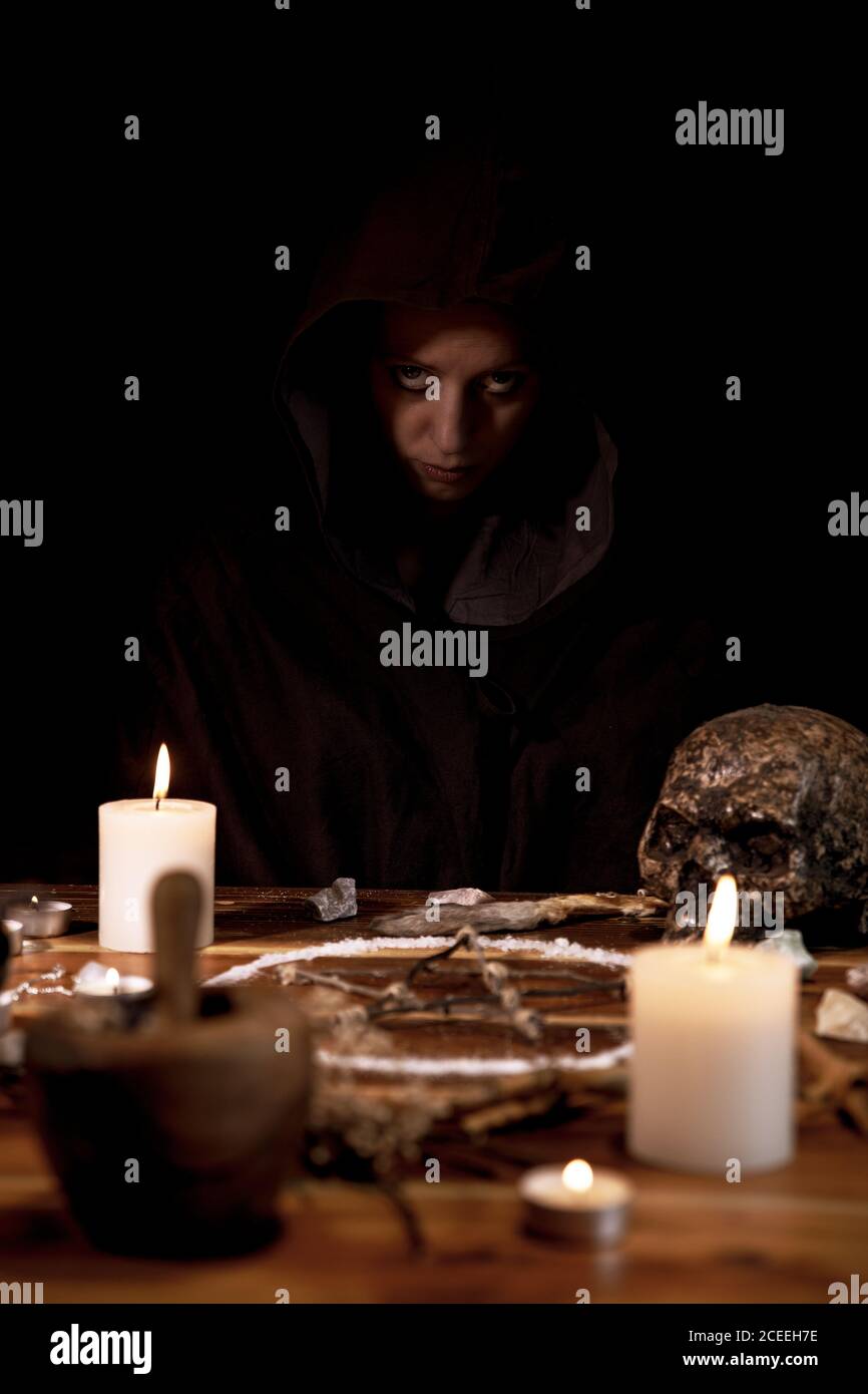 Woman sitting in the dark background of an occultism ritual table, pentagram, candles and a skull, copyspace Stock Photo
