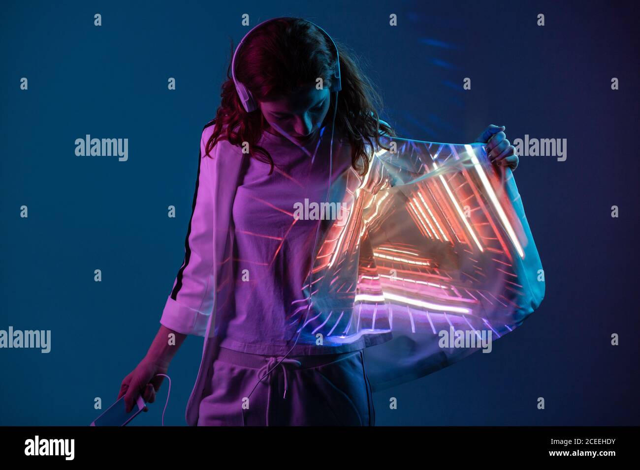 Young woman in headphones looking at neon light projection on blazer in studio Stock Photo