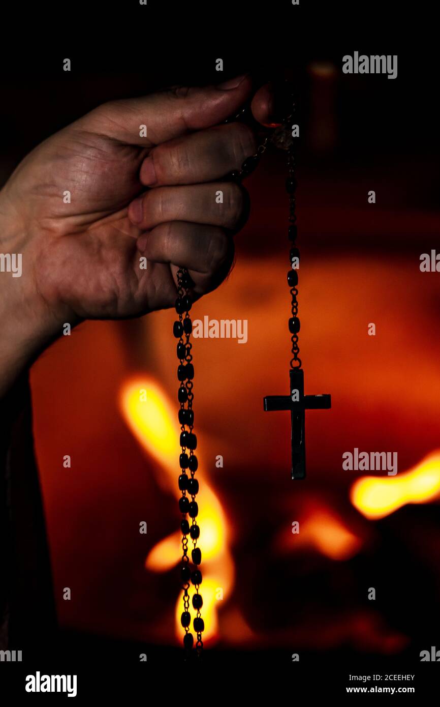 Prayer holding a crucifix or holy rosary beads, religion and praying, fire background in the dark, bodypart hand Stock Photo
