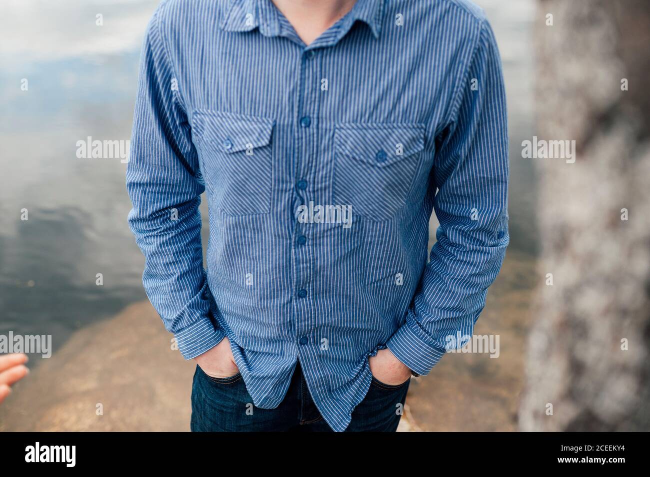 Crop unrecognizable man with hands in pockets standing at the water. Stock Photo