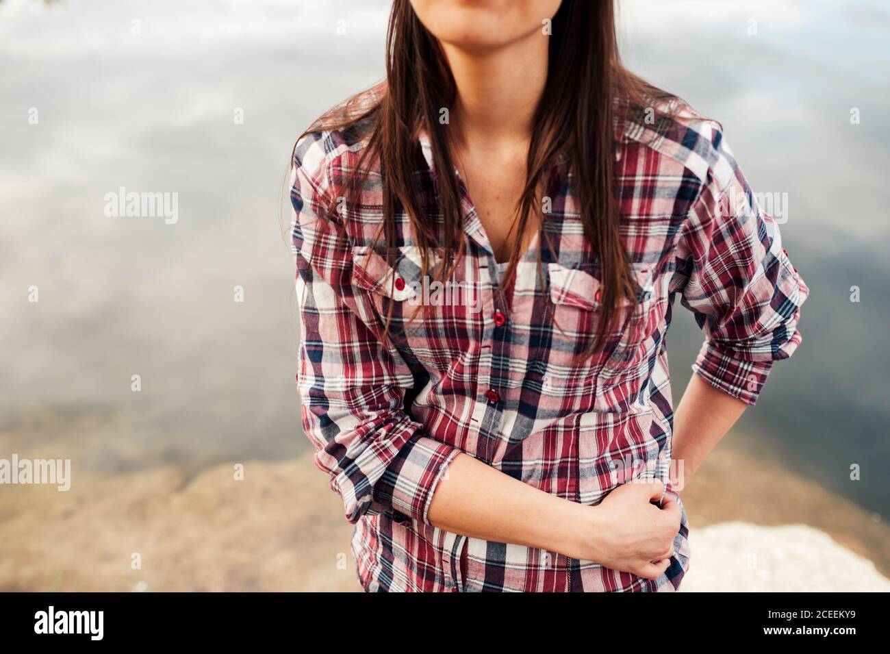 Crop unrecognizable Woman with hands in pockets standing at the water. Stock Photo