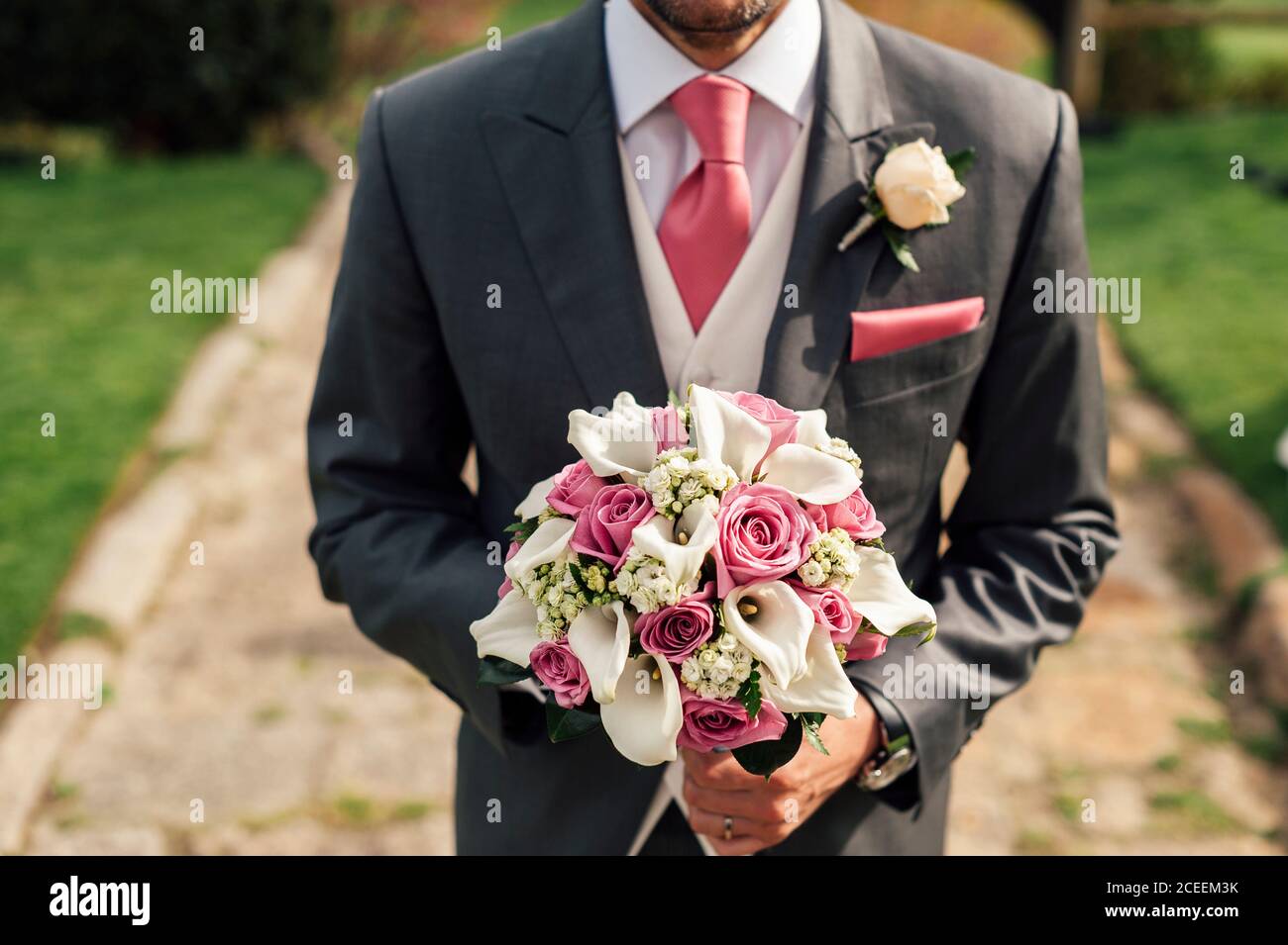 Crop handsome man in gray suit standing with bunch of pink and white flowers. Stock Photo