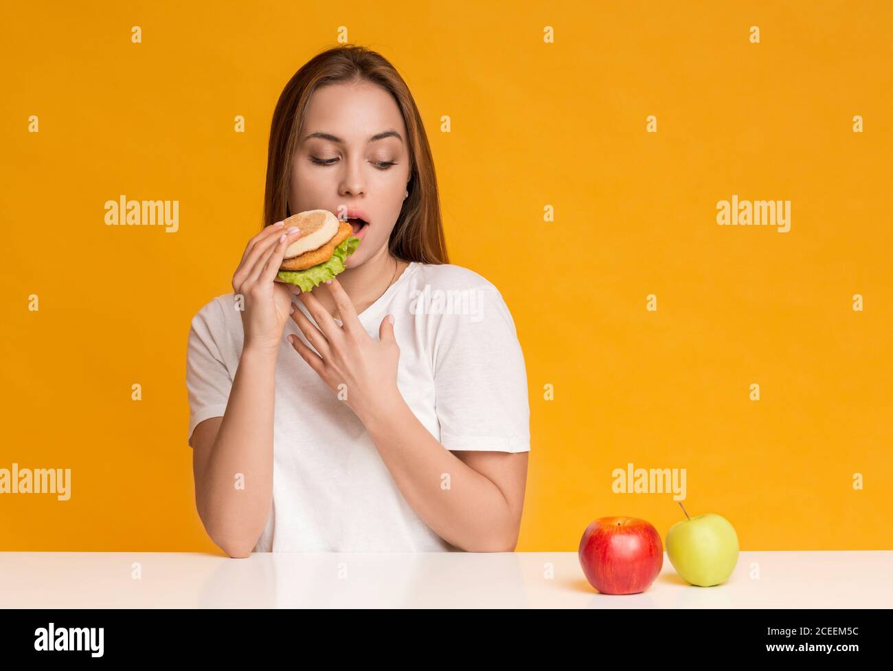 Hungry Girl Eating Unhealthy Burger Instead Of Apple Fruit Stock Photo