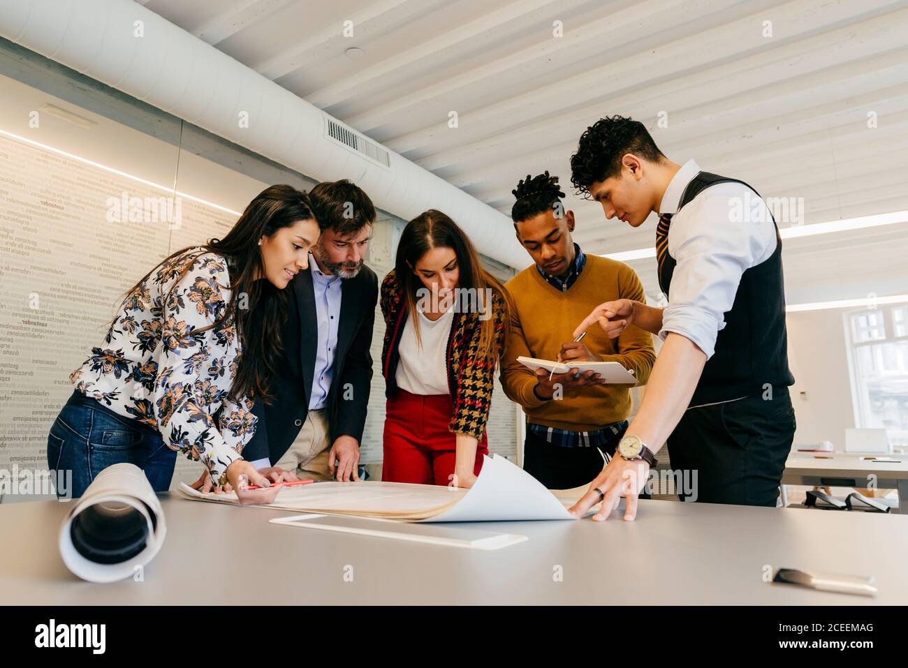 Multiethnic office team standing at the table while working on the blueprint. Stock Photo