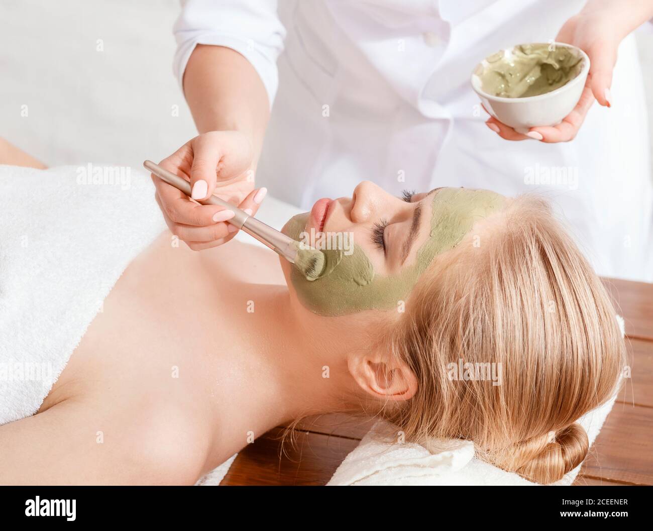 Facial and beauty. Beautician smears client face with clay Stock Photo