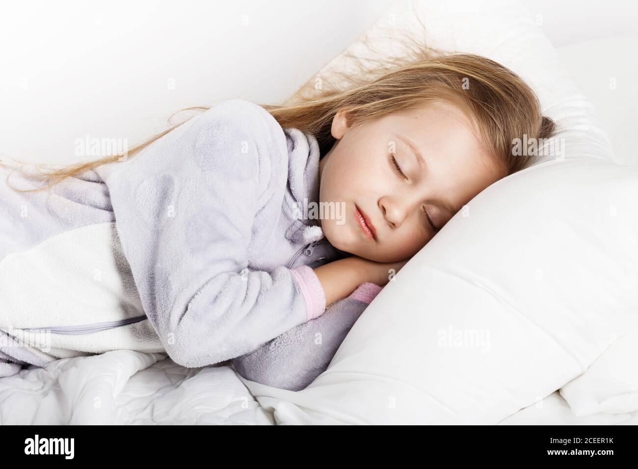 Adorable little girl sleeping in the bed in warm pajamas against white background Stock Photo