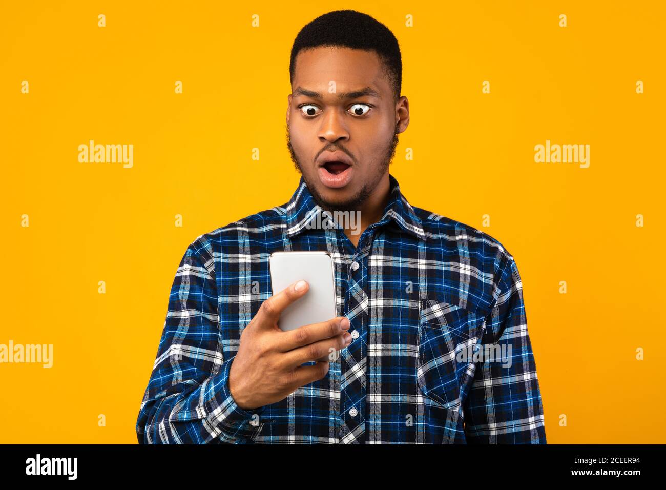 Shocked Black Man Looking At Smartphone Reading SMS, Yellow Background Stock Photo