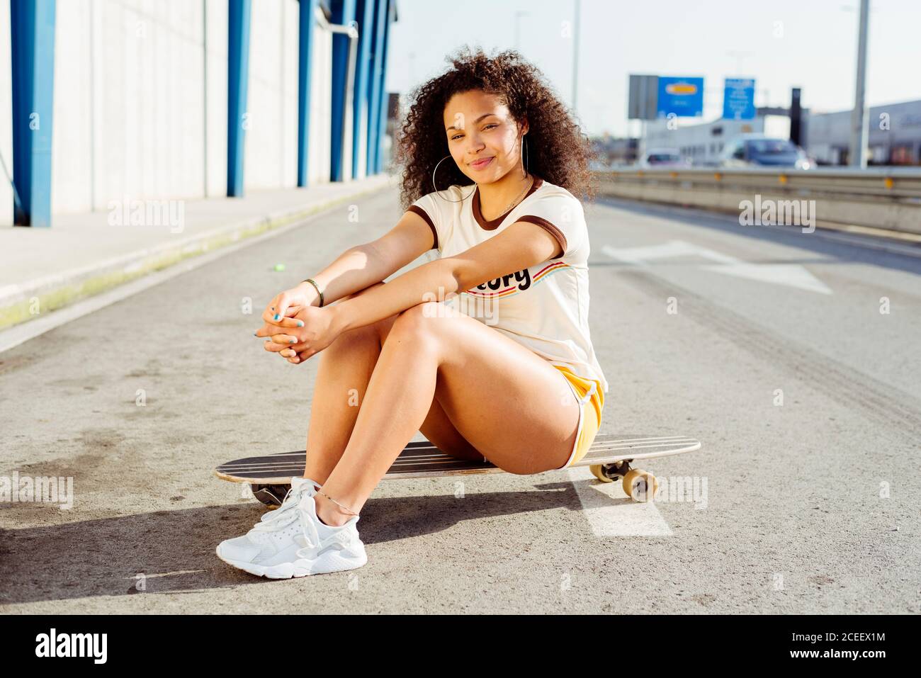 African-American teenager sitting on skateboard on road Stock Photo