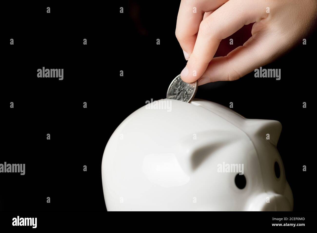 Child’s hand putting a quarter into a piggy bank.  Saving money concept, black background Stock Photo