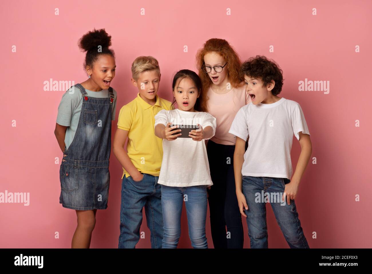 Surprised schoolkids watching shocking news on smartphone over pink background Stock Photo