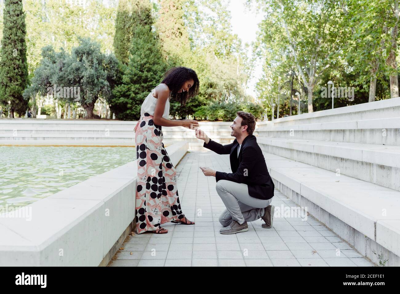 Side view of handsome Caucasian man proposing to African-American lady while spending time in park together Stock Photo