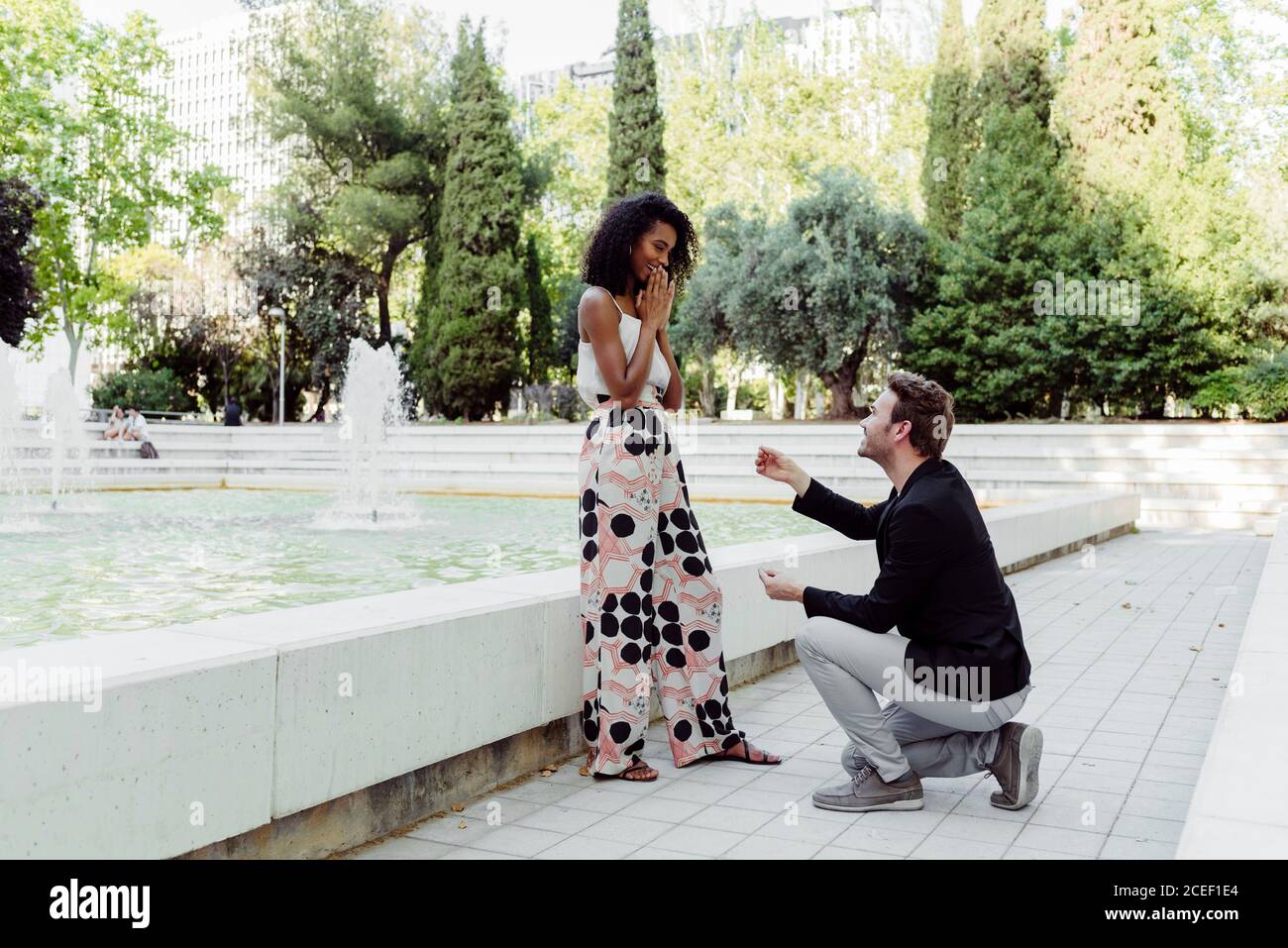 Side view of handsome Caucasian man proposing to African-American lady while spending time in park together Stock Photo