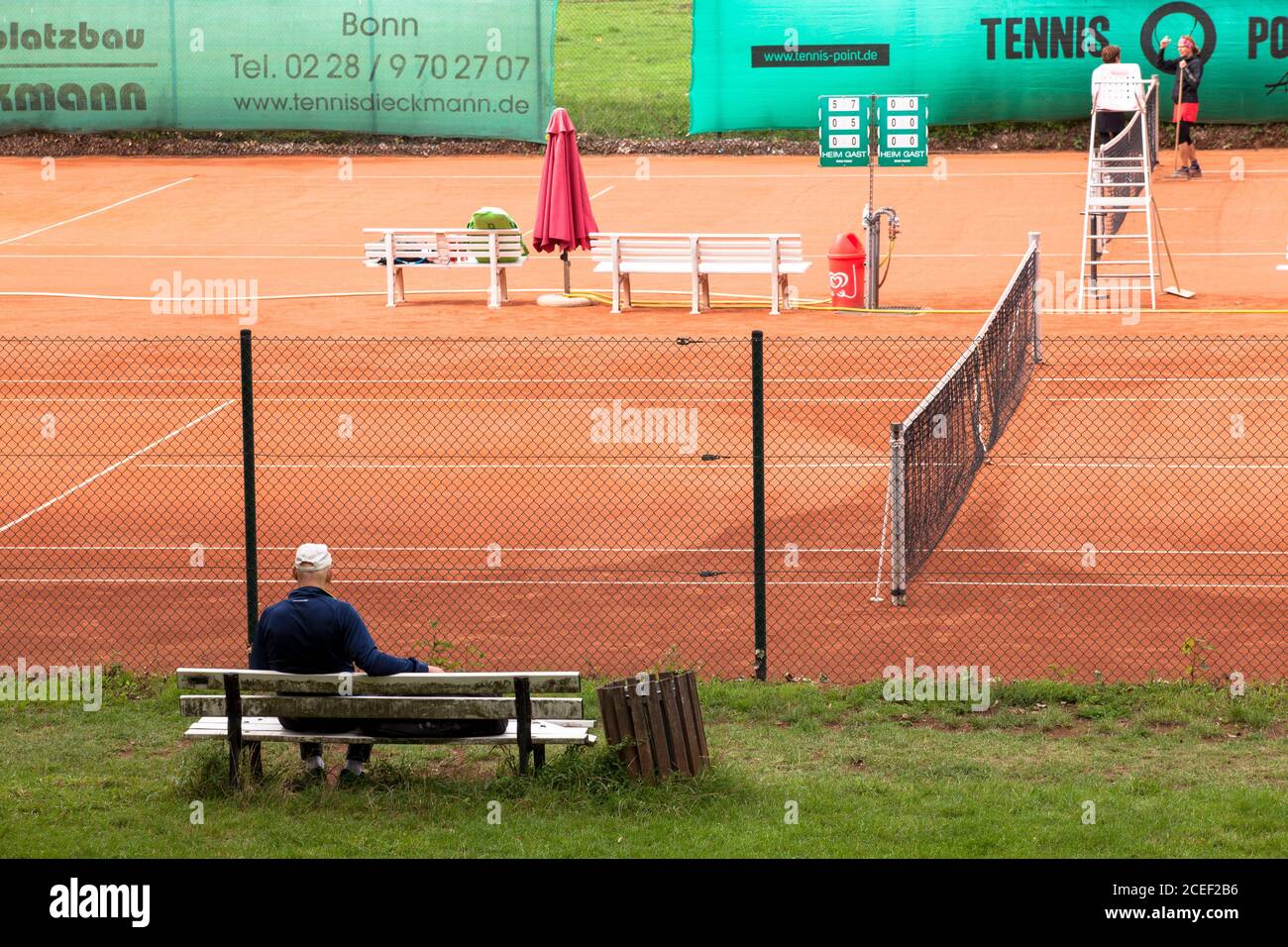 man sitting on a bench in front of a tennis court at the Rhine meadows in the district Poll, Cologne, Germany.  Mann sitzt auf einer Bank vor einem Te Stock Photo