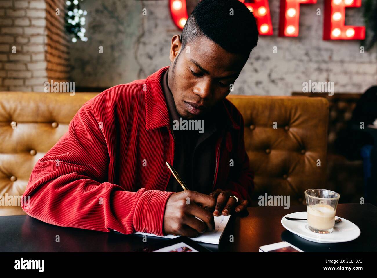 Serious african male in red jacket letter at table in cafe Stock Photo
