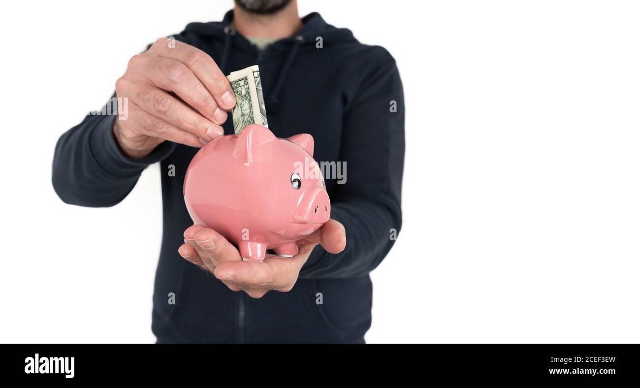midsection of man holding piggy bank in one hand and inserting dollar bill into it with the other Stock Photo
