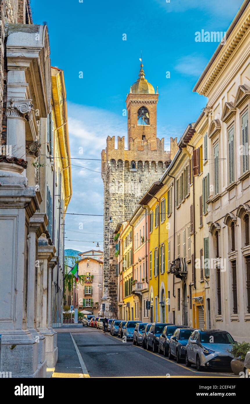 Typical italian street with parked cars and Torre della Pallata brick medieval tower building background, Brescia city historical centre, vertical view, Lombardy, Northern Italy Stock Photo