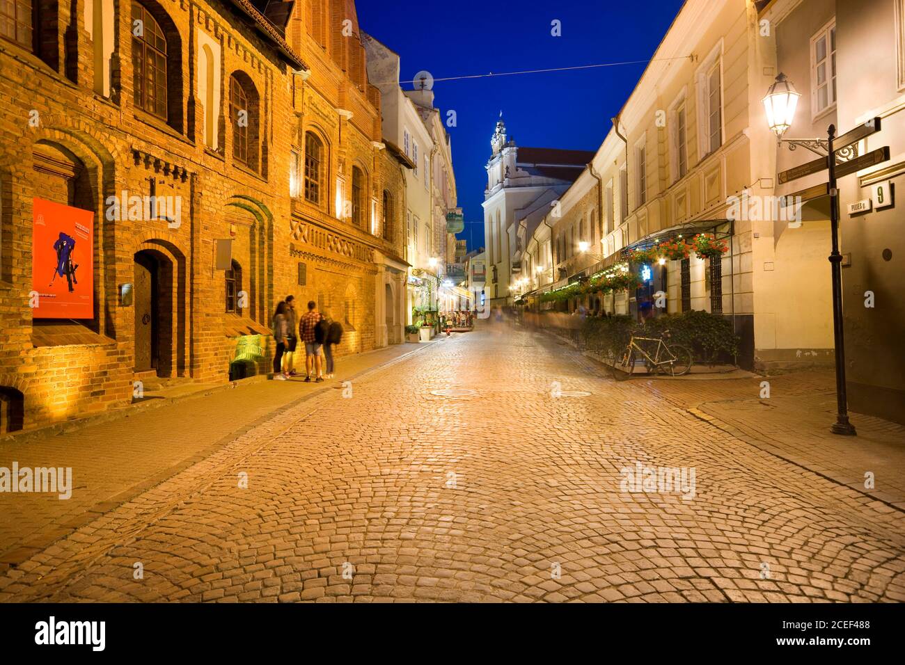 Night view of illuminated Pilies Street in the Old Town of Vilnius, Lithuania. Church of St. Johns in the background. Stock Photo