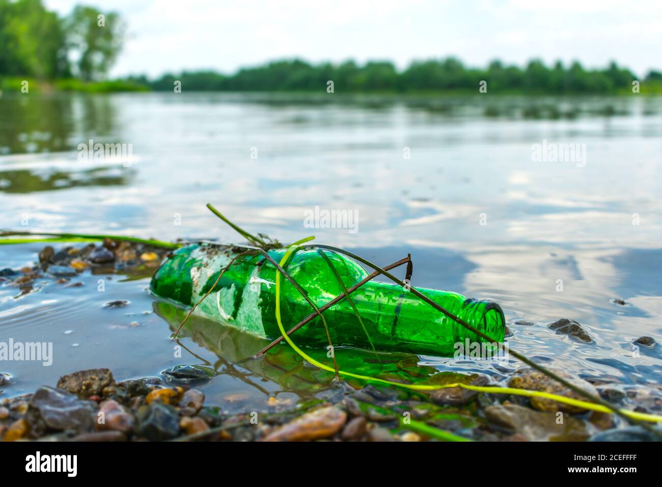 Glass bottle on the riverbank pollutes the environment. Nature pollution with garbage left by vacationers on the beach Stock Photo