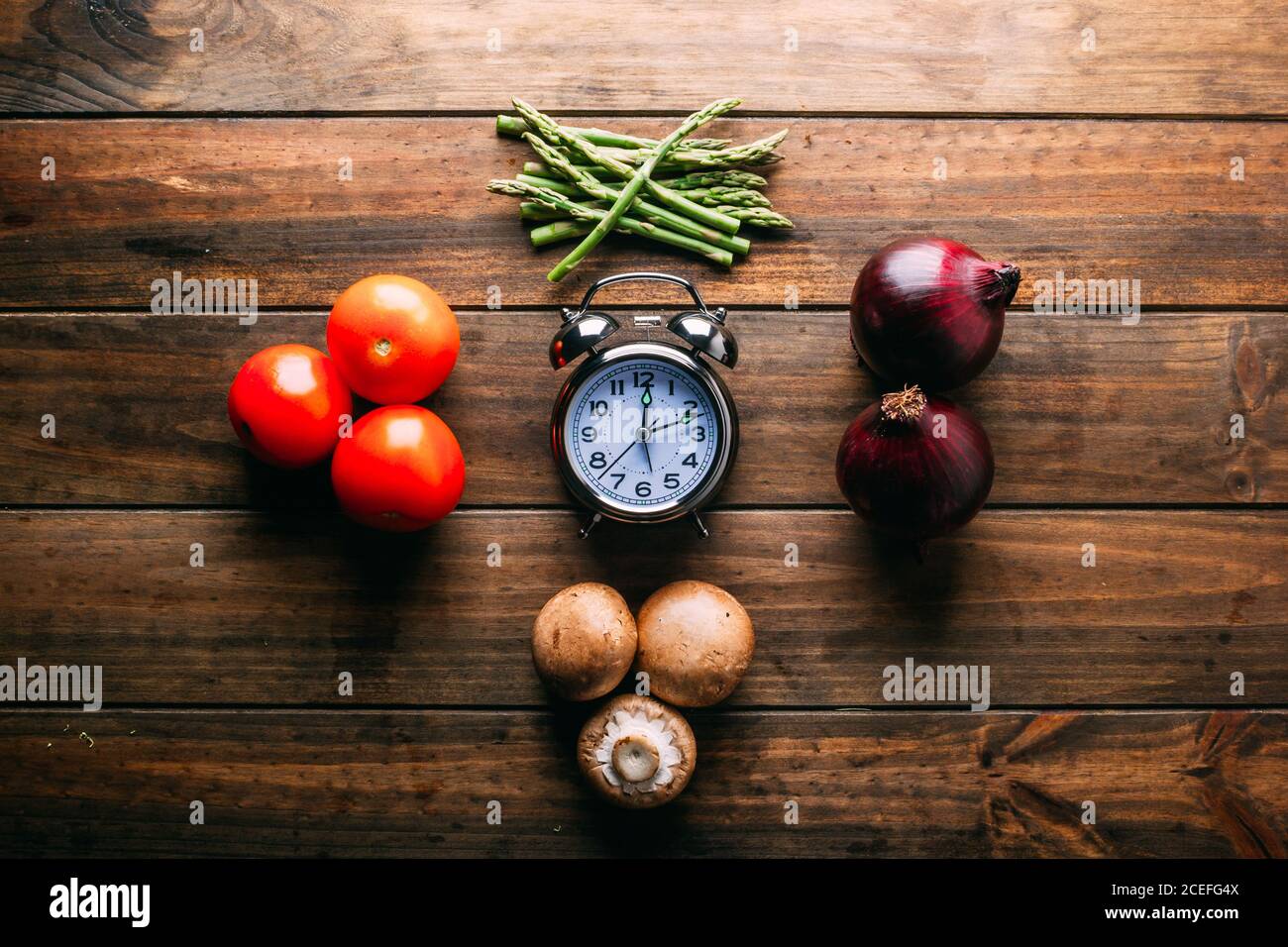 Assorted fresh vegetables and bottle of oil lying on timber tabletop near various cooking tools Stock Photo