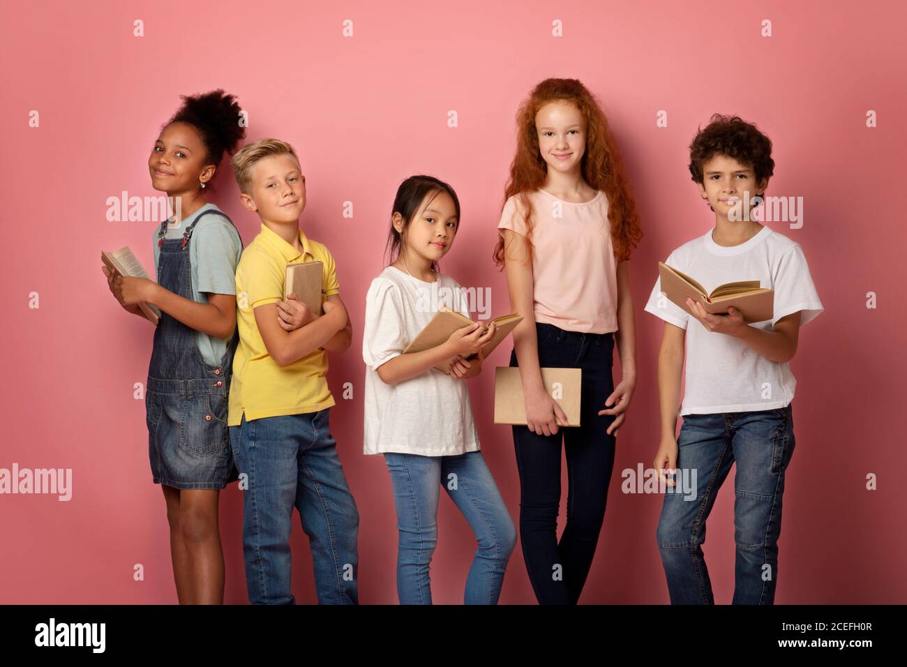 Multinational schoolkids with textbooks looking at camera over pink background, portrait Stock Photo