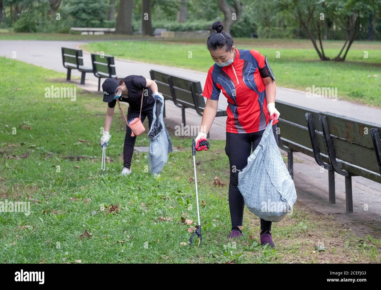 Two Asian American volunteers wearing face masks clean Kissena Park. In Flushing, Queens, New York City. Stock Photo
