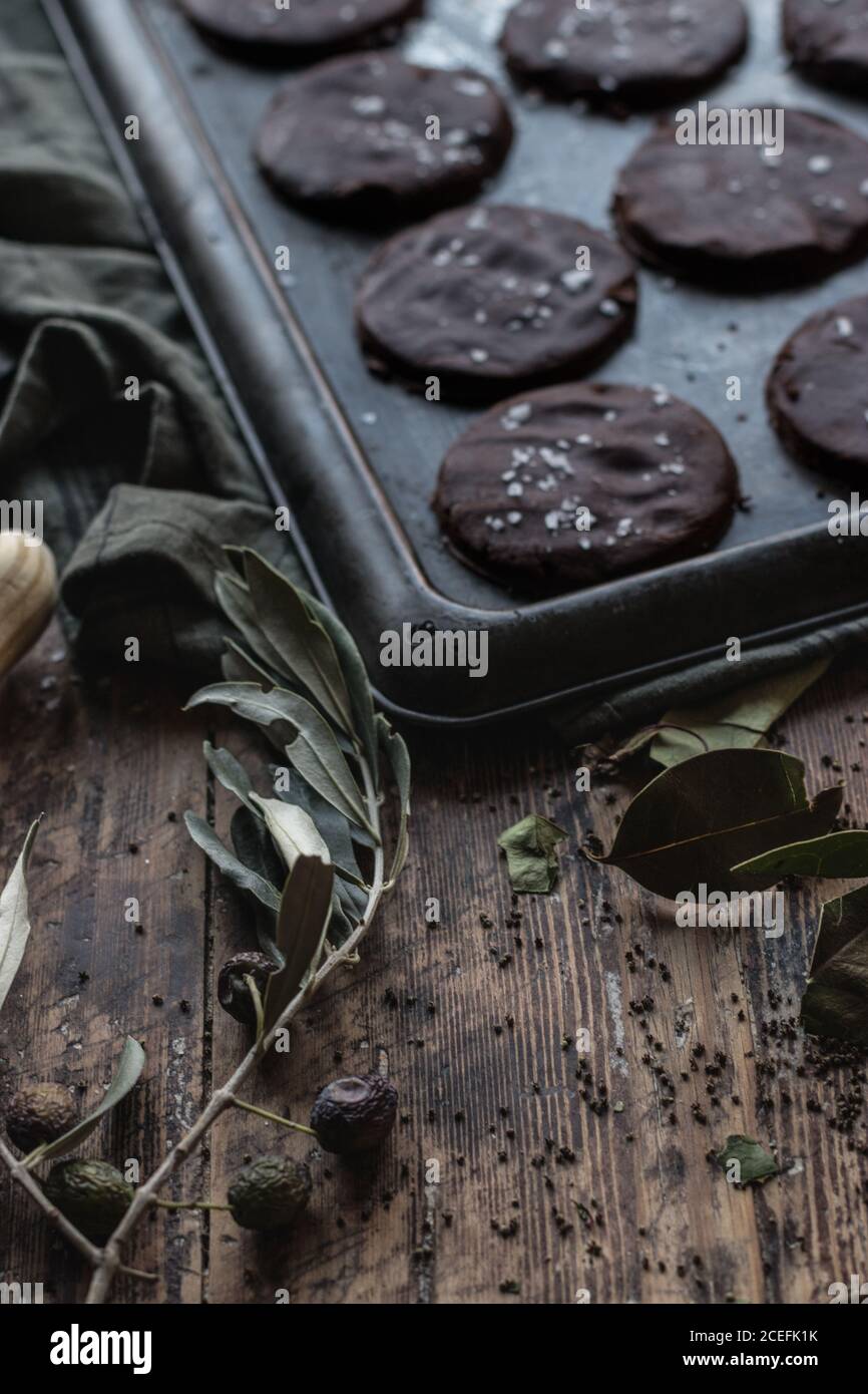 Dry olive branch lying near baking pan with set of yummy gluten free chocolate cookies on shabby timber tabletop Stock Photo