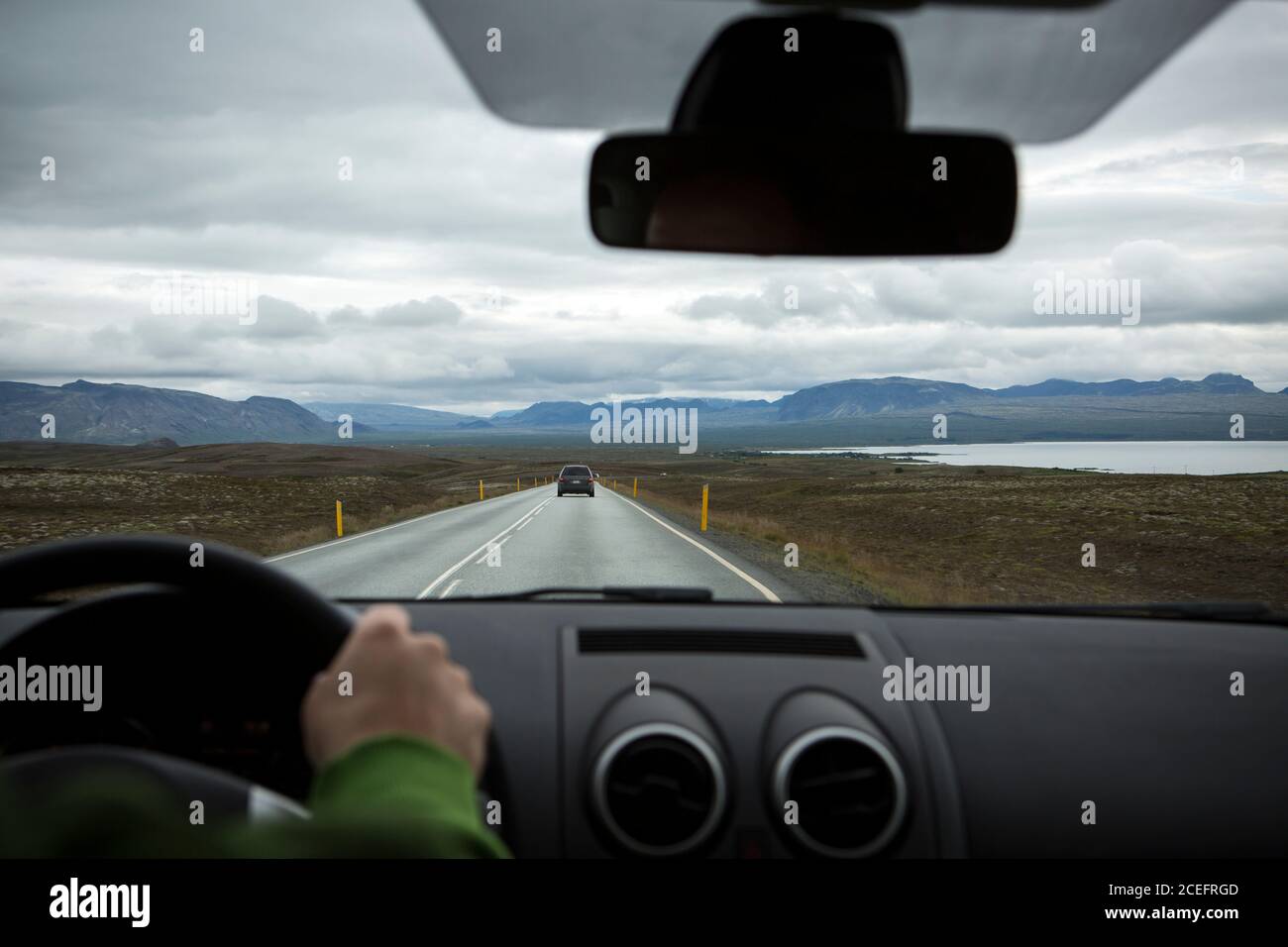 Crop view of person's hand driving automobile on road passing between water, dale and hills in Iceland Stock Photo