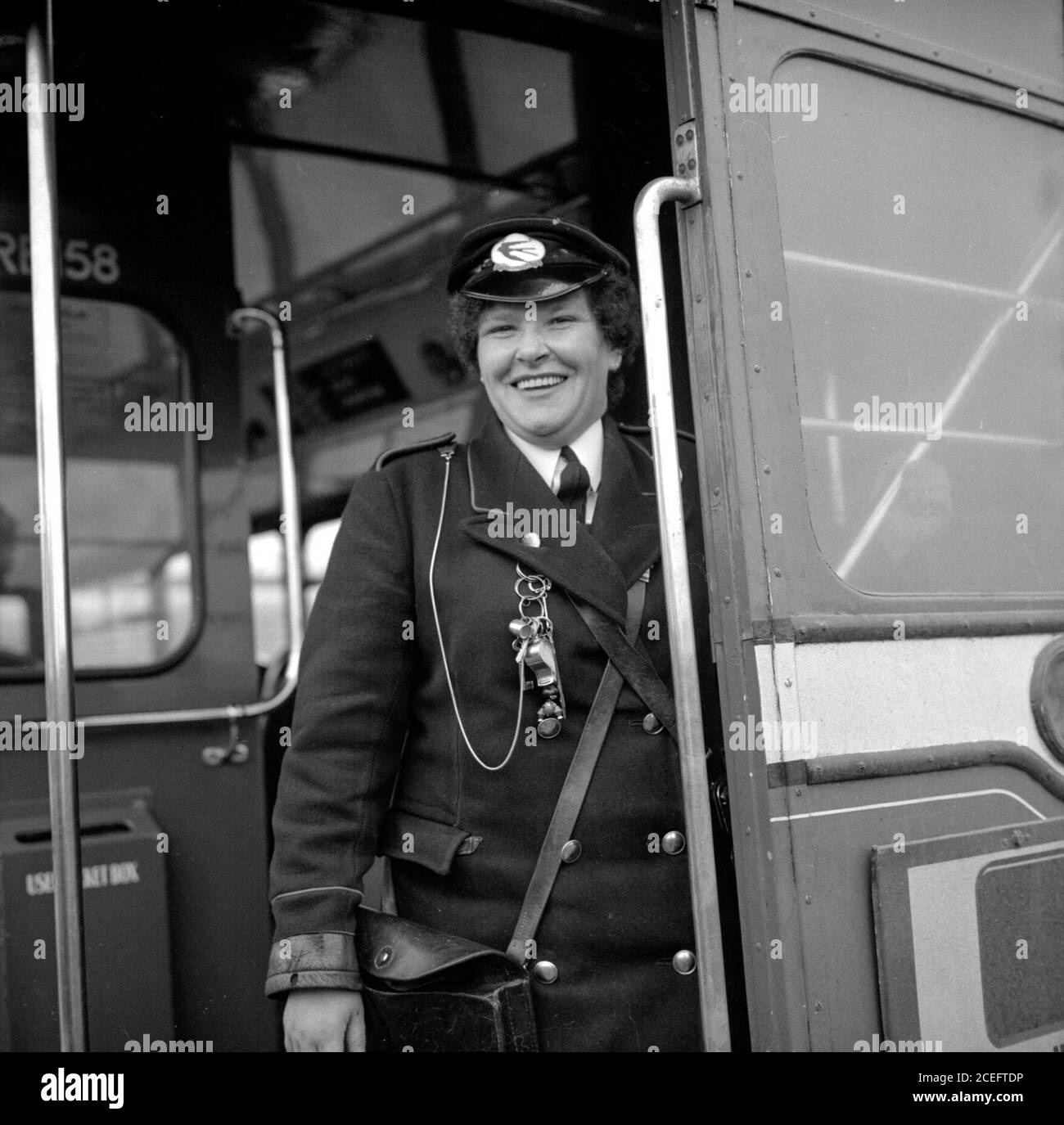 A bus conductress in Fife, Scotland smiles as she stands at the back of her routemaster bus in the 1950s, before she rings the bell to signal that the driver can drive on Stock Photo