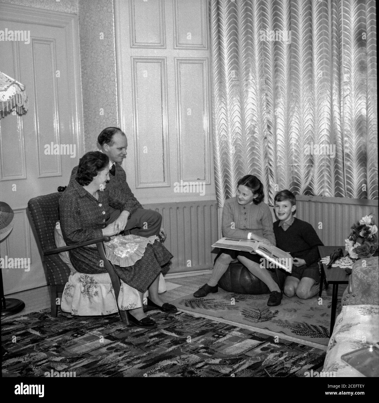 A Scottish couple relax in their living room with their two young children, kept warm by their new coal fired central heating system, in the 1950s Stock Photo