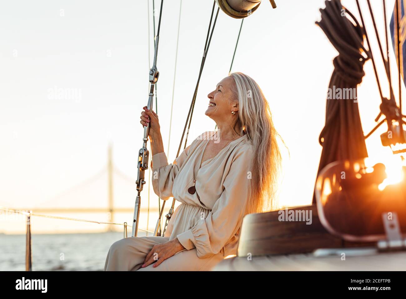Side view of mature woman with long hair sitting on yacht and smiling Stock Photo