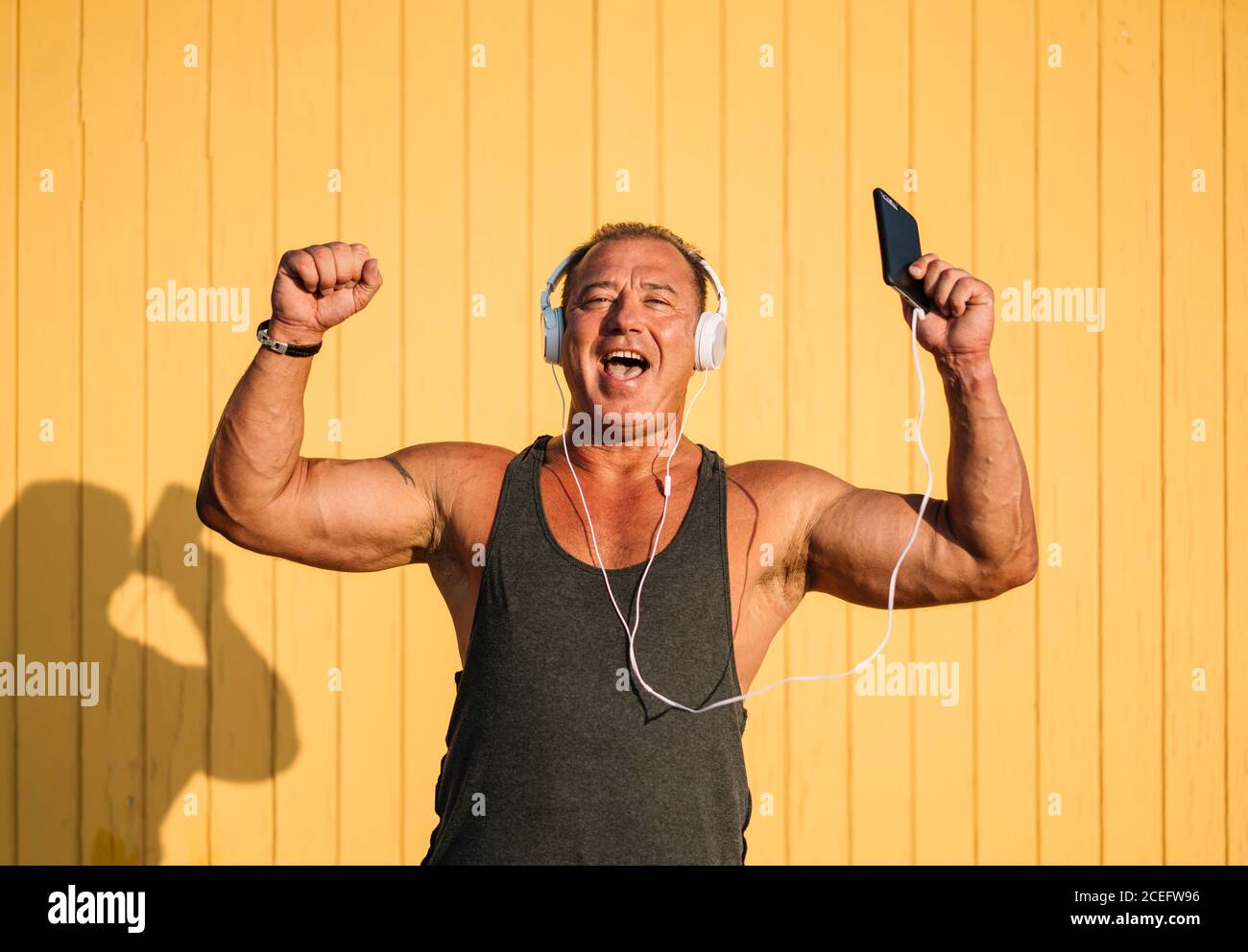 Strong older man poses with headphones on yellow background. Stock Photo