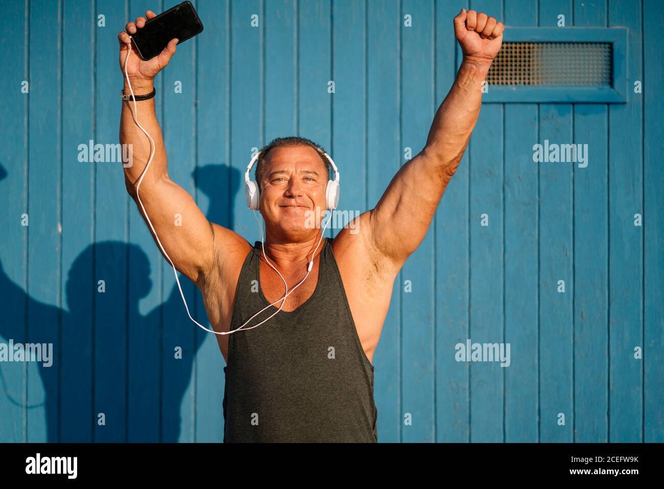 Strong older man poses with headphones on blue background. Stock Photo