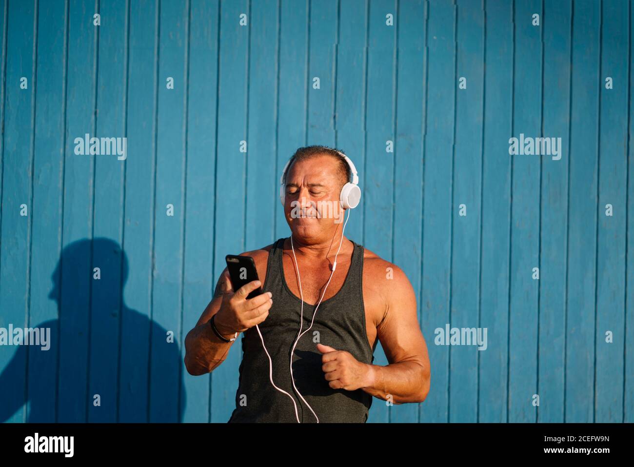 Strong older man poses with headphones on blue background. Stock Photo