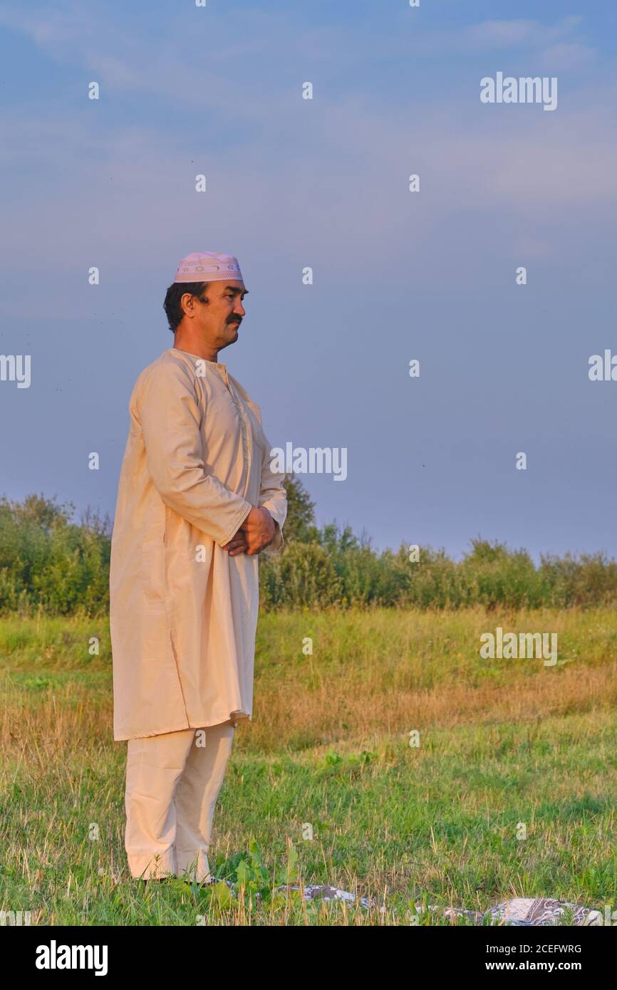 A muslim senior man wearing a skullcap and traditional clothes prays Portrait of a cute young black bull on a pasture Stock Photo