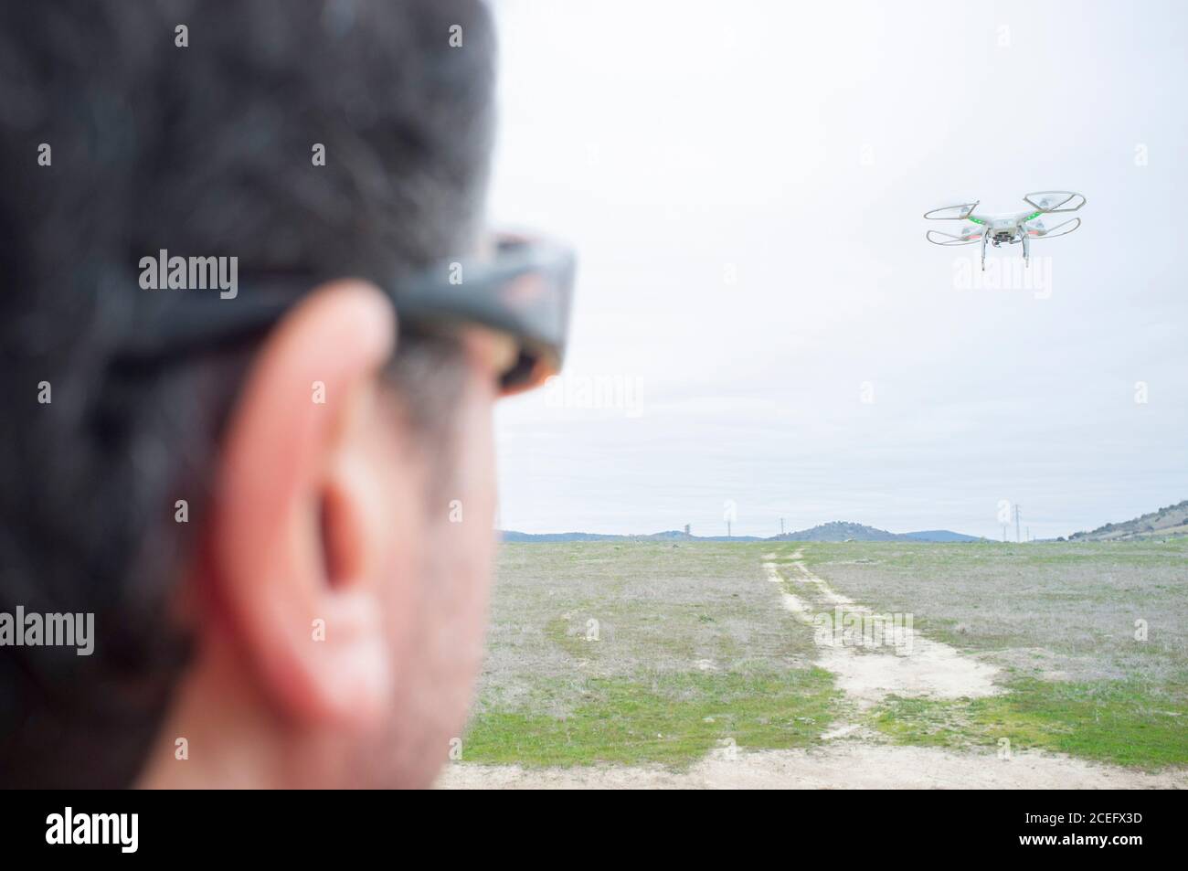 Pilot flying drone on aproaching maneuver. He is maintaining visual contact with UAV on air at all times Stock Photo