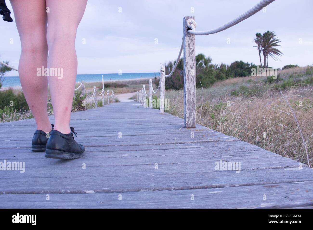 piernas de una chica joven caminando por la pasarela de madera que le lleva directa a la playa ( en el saler, valencia) Stock Photo