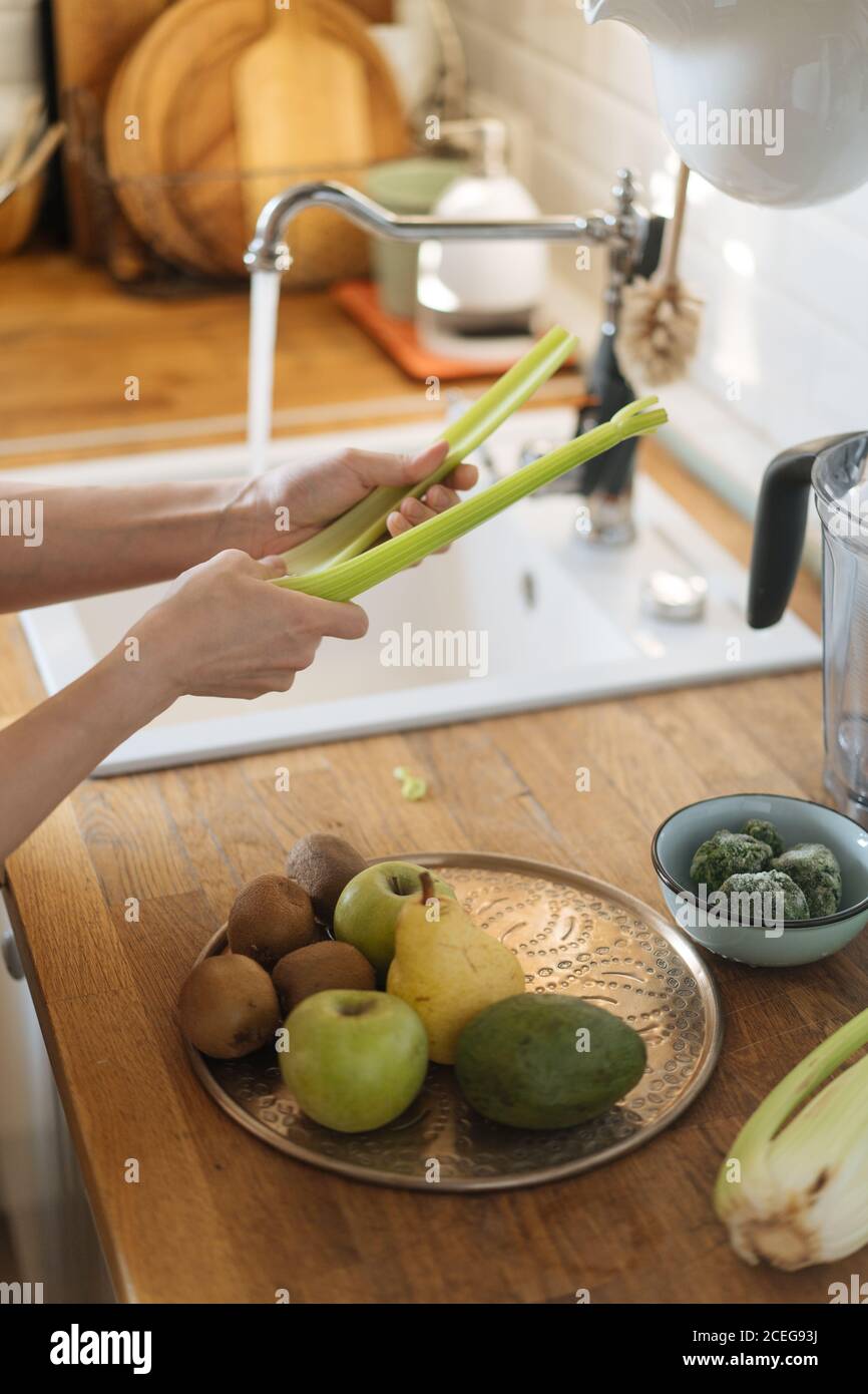 Side view of Woman washing green vegetables in sink under stream of