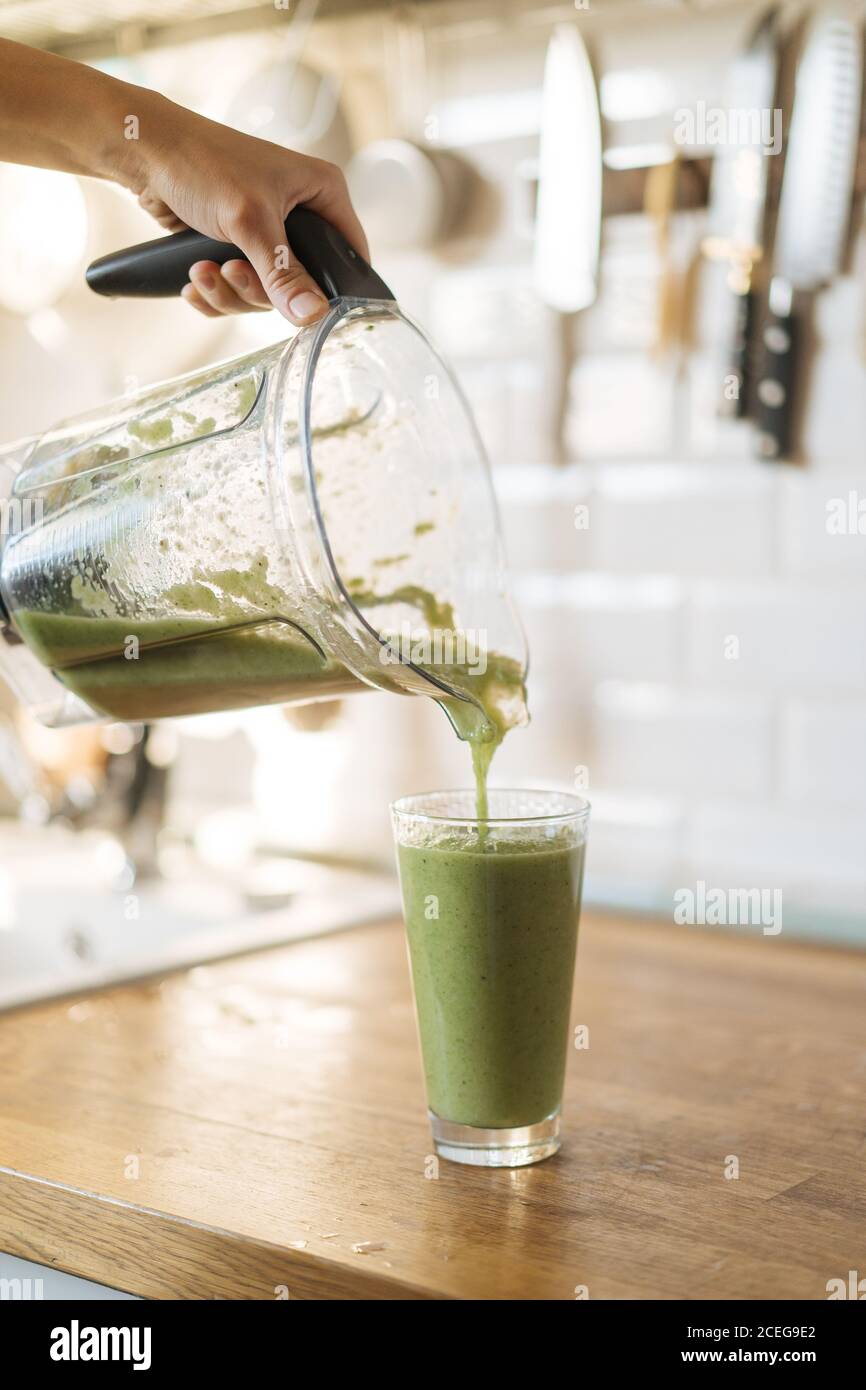 Crop female hand pouring healthy green smoothie from blender cup into