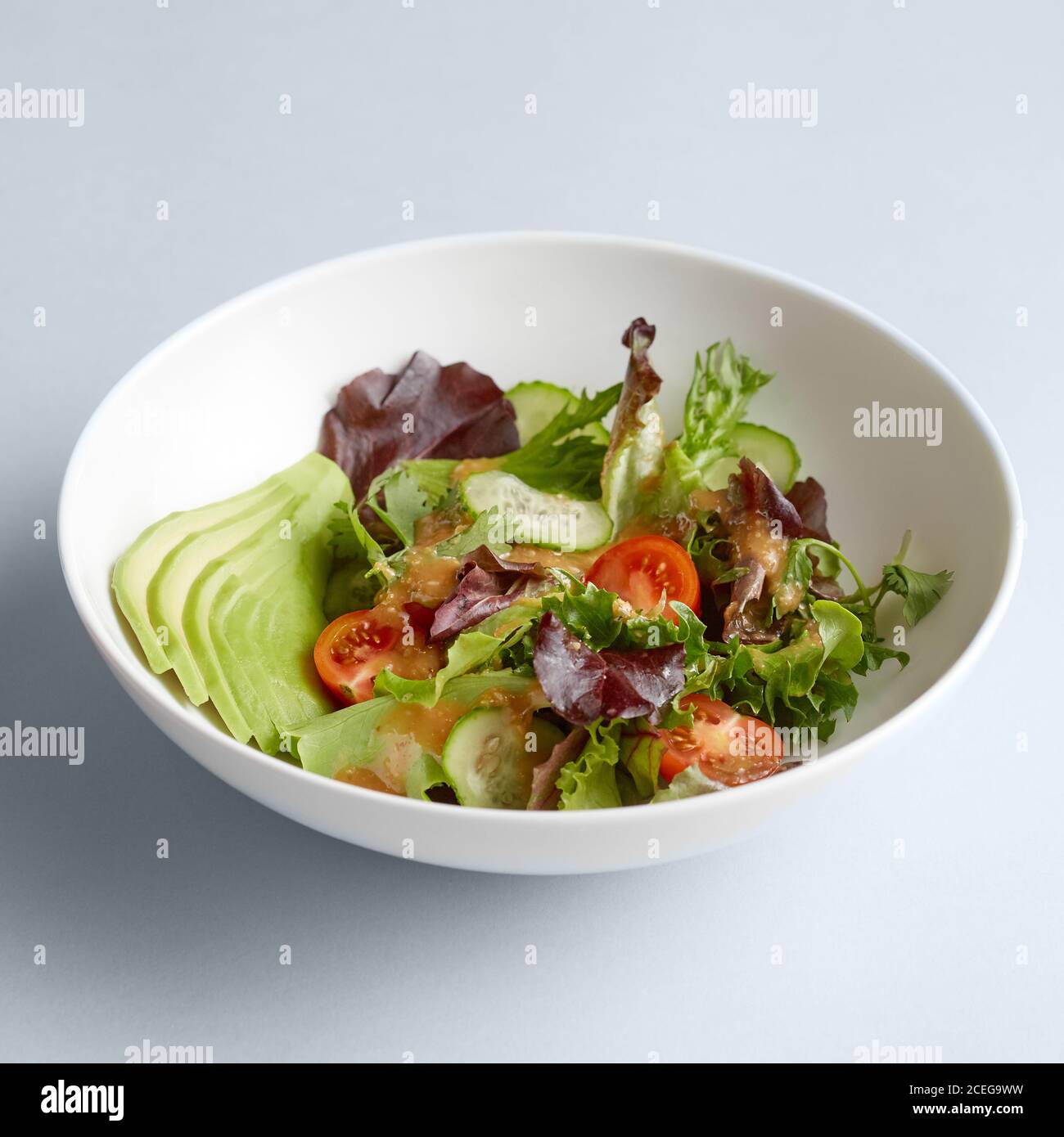 Beautiful chopped cucumbers, tomatoes and potherbs mixed in large ceramic white bowl on white background Stock Photo