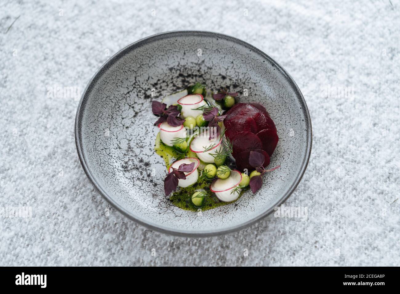 Beautiful grey bowl with mixed chopped potherbs, peas and vegetables served on grey textured?cloth from above Stock Photo