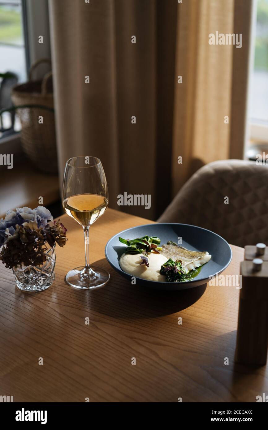 Flat lay of blue plate with fish fillet and sauce with green in Nordic style served with white wine Stock Photo