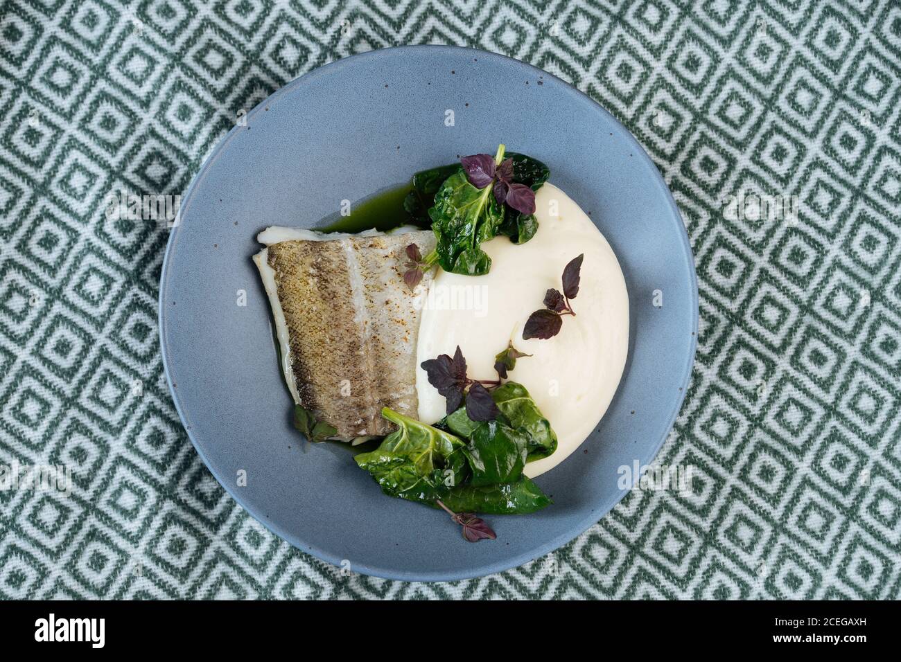 Flat lay of blue plate with fish fillet and sauce with green in Nordic style served on fabric Stock Photo