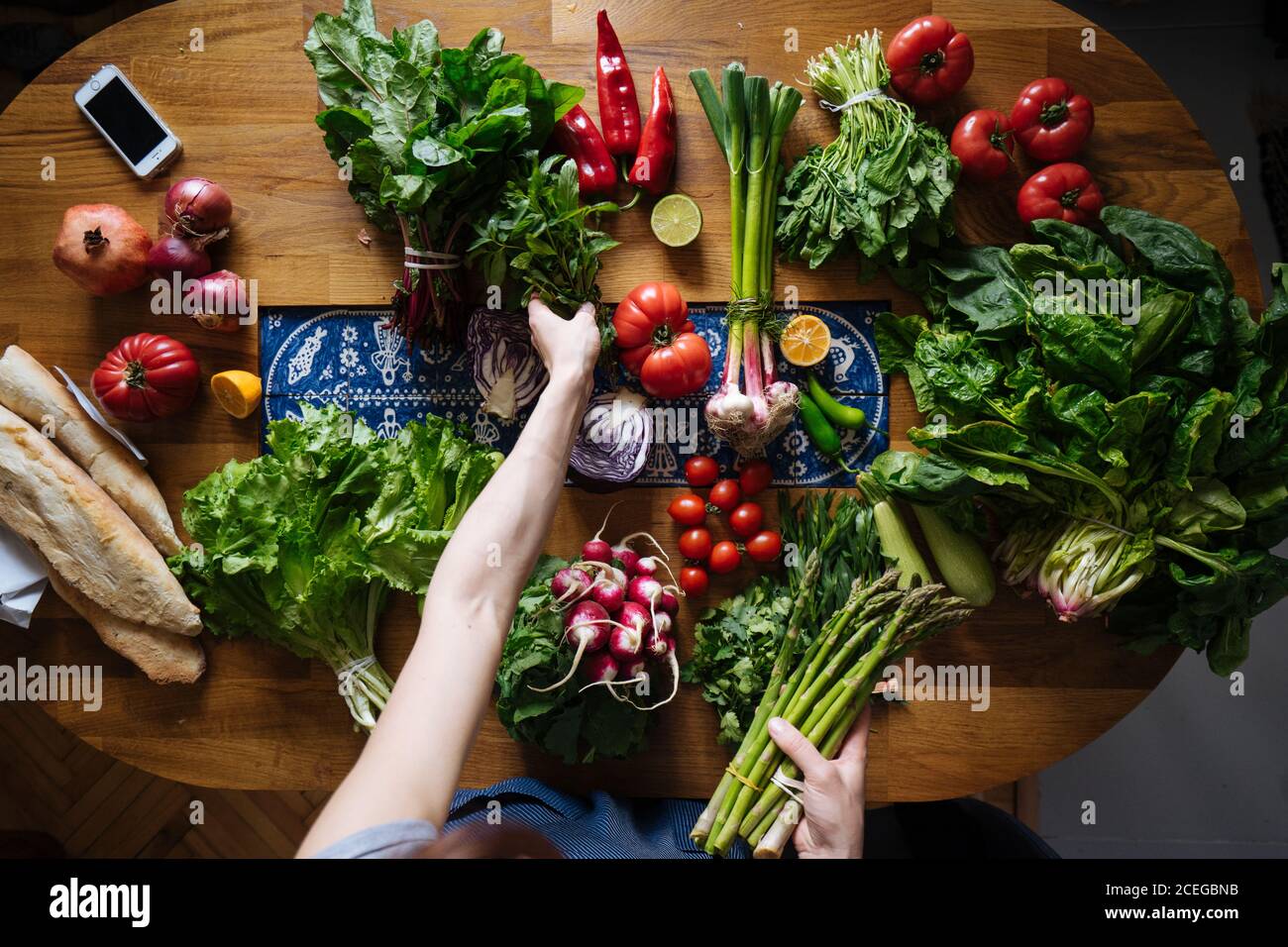 Crop view of female hands taking potherbs from elegant table with fresh healthy vegetable and fruit cooking ingredients from above Stock Photo